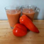 Gaspacho à la courgette sans gluten, servi dans des verres avec des tomates en arrière-plan.