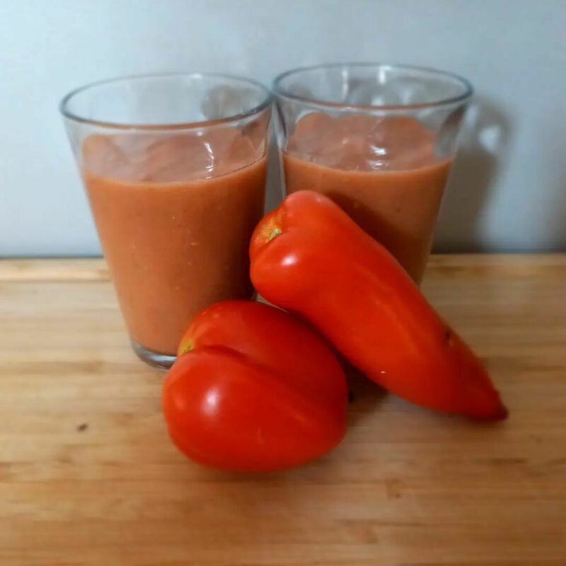 Gaspacho à la courgette sans gluten, servi dans des verres avec des tomates en arrière-plan.