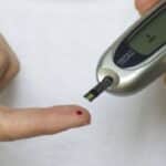 Personne mesurant son taux de glucose dans le sang avec un glucomètre, illustrant le lien entre la consommation de fécules et le diabète.