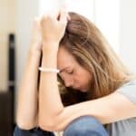 Femme en détresse tenant sa tête avec les mains, symbolisant la découverte de son intolérance au gluten.