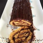 Photo d'une bûche de Noël sans gluten enrobée de chocolat, posée sur une assiette décorative.