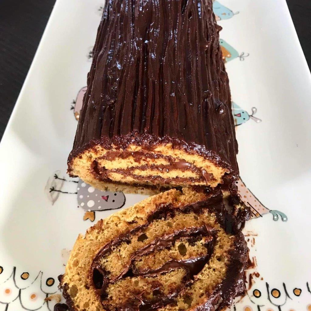 Photo d'une bûche de Noël sans gluten enrobée de chocolat, posée sur une assiette décorative.