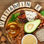 Aliments riches en vitamine E, y compris avocat, noix et graines, disposés en cercle avec des lettres formant le mot 'VITAMINE
